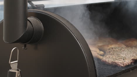 Pan-to-BBQ-pit-smoker-lid-being-opened-in-slow-motion,-reveals-pork-ribs-and-chicken-thighs