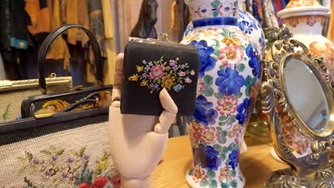 Eine-Künstliche-Hand-Aus-Holz-Hält-Eine-Brieftasche,-Im-Hintergrund-Bunte-Vasen