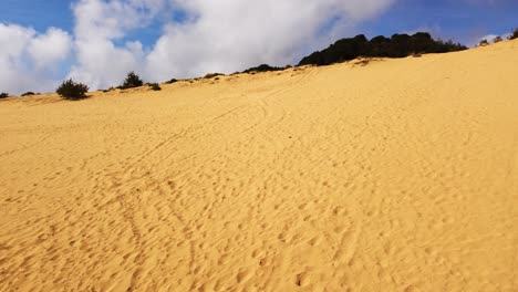 Desert-dune-landscape,-golden-sand-with-footsteps,-sunny-white-clouds-background