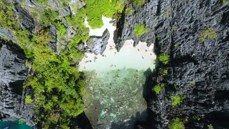 Aerial-View-:-tourists-swimming-in-the-secret-beach,-a-tropical-shallow-lagoon-surrounded-by-Karst-cliffs