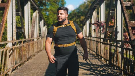 Young-man-traveler-with-backpack-walking-on-rusty-old-bridge-outdoors-on-sunny-summer-day-in-slow-motion