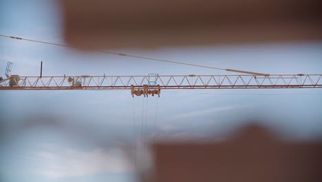 Detail-of-the-arm-of-a-yellow-construction-crane-in-motion-seen-through-out-of-focus-foreground-objects