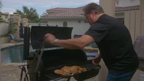 Man-puts-raw-chicken-thighs-on-to-grill-in-smoking-BBQ-pit