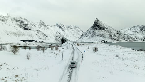 Aerial-View-Of-Campervan-Driving-On-The-Snowy-Road-To-Fredvang-Bridges-In-Winter-In-Lofoten-Island,-Norway