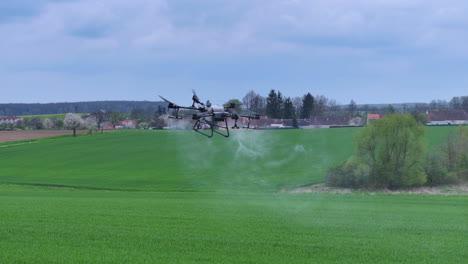 Agricultural-Drone-Flying-and-Spraying-Fertilizer-on-Green-Farming-Field,-Tracking-Aerial-View