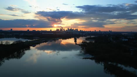 Luftaufnahme-Des-Sonnenuntergangs,-Blick-Auf-Die-Skyline-Des-Stadtzentrums-Von-Warschau-Und-Ihre-Spiegelung-Auf-Dem-Fluss-Mit-Wunderschönen-Orangetönen-Und-Wolken