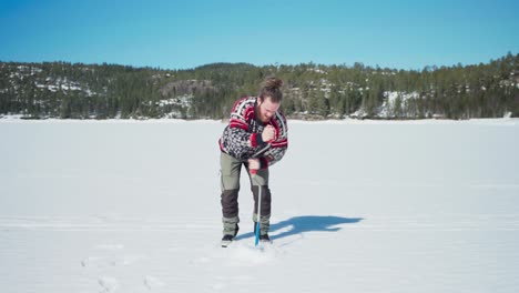 Person-Drilling-A-Hole-In-The-Frozen-Lake-For-Ice-Fishing-During-Sunny-Winter-Season