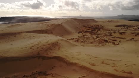 Huge-sand-dunes-scenery-at-shore,-aerial-sideway-shot,-partly-cloudy-day