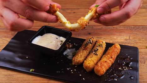 Close-up-of-a-plate-of-cheese-fingers-breaded-with-sesame-seeds,-habanero-peppers,-ranch-dressing-and-Worcestershire-sauce,-cheese-finger-being-halved-and-then-dipped-in-ranch-dressing