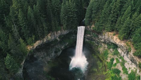 Aerial-Flying-Overhead-Cascading-Waterfall-Surrounded-By-Tall-Coniferous-Forest-Trees