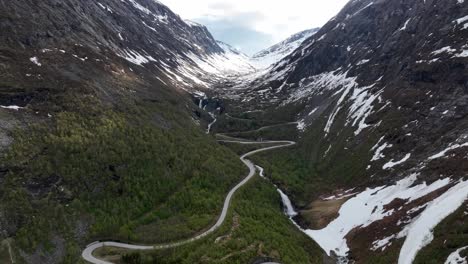 Curvy-winding-road-Strynevegen-leading-to-Old-Strynefjellet-mountain-crossing---Norway-springtime-aerial-with-beautiful-waterfall-close-to-road