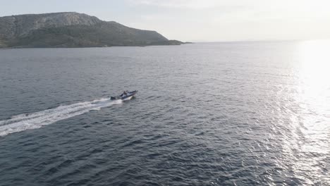Aerial-tracking-shot-of-speedboat-speeding-over-blue-ocean-during-sunset-time---Mountain-in-background---Greece,Europe
