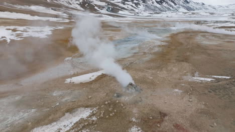 Luftaufnahme-Des-Aktiven-Geothermiegebiets-In-Der-Isländischen-Landschaft,-Dämpfe,-Schlammtöpfe-Und-Schneebedeckte-Hügel