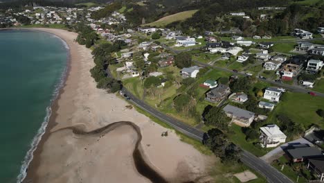 Aerial-birds-eye-view---road-beside-sandy-beach,-small-waterfront-settlement-of-Langs-Beach,-New-Zealand