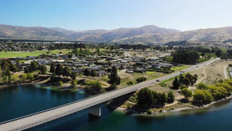 Drone-aerial-view-of-light-traffic-on-a-bridge-and-road-by-sunny-Cromwell,-small-town-on-South-island-of-New-Zealand