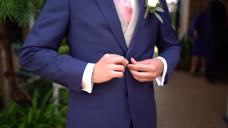 Slow-motion-shot-of-Groom-fastening-the-buttons-on-his-blue-jacket-suit,-Tracking-motion