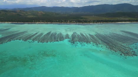 Aerial-dolly-in-above-crystal-waters-towards-buildings-of-Domaine-de-Deva,-New-Caledonia