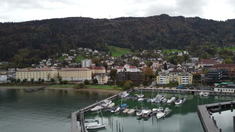 Aerial-view-of-the-historic-city-of-Bregenz-on-the-shore-of-Lake-Constance-on-a-cloudy-happy-autumn-day-surrounded-by-hills-and-with-the-boats-in-the-port,-without-people,-Vorarlberg,-Austria,-Europe
