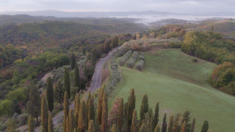 Rural-woodland-road-passing-through-scenic-Tuscany-landscape,-aerial