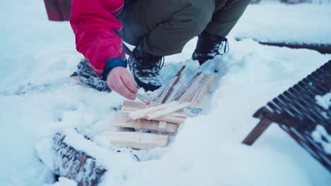 Man-Making-Fire-On-Chopped-Wood-In-The-Snow-During-Winter