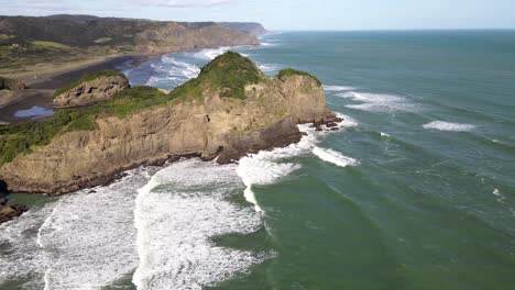 Aerial-reveal-of-wild-New-Zealand-coastal-scenery-with-black-sand-beach-and-volcanic-rock-formations