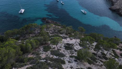 Drone-view-of-descending-cliffs-and-looks-Sailboats-Docked-in-Cala-d-egos-Beach