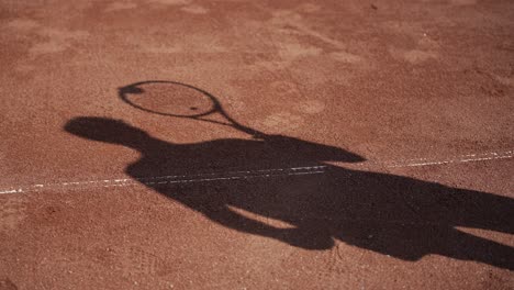 Jugador-De-Tenis-De-Silueta-De-Sombra-Rebotando-La-Pelota-En-La-Raqueta,-Cancha-De-Juego-Roja-Usada