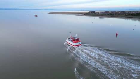 Fishing-trawler-heading-out-to-sea-on-calm-water-at-dusk-on-River-Wyre-Estuary-Fleetwood-Lancashire-UK-with-Knott-End
