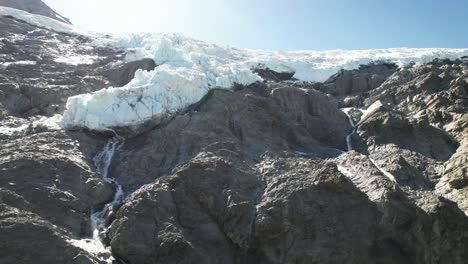 Aerial-close-up-of-hanging-glacier-from-mountain-top-melting-down-in-waterfalls