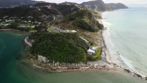 Aerial-pull-back-reveal-of-Mangawhai-Heads,-houses-and-popular-sandy-beach