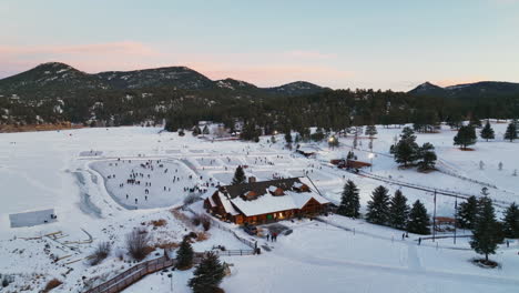 Evergreen-Lake-house-January-mid-winter-ice-skating,-pond-hockey-and-ice-fishing-under-lights-sunset-Colorado-circle-left-cinematic