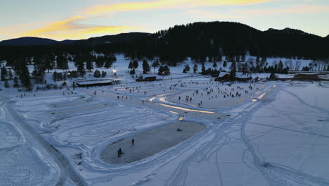 Evergreen-Lake-house-January-mid-winter-ice-skating,-pond-hockey-and-ice-fishing-under-lights-sunset-Colorado-cinematic-circle-right