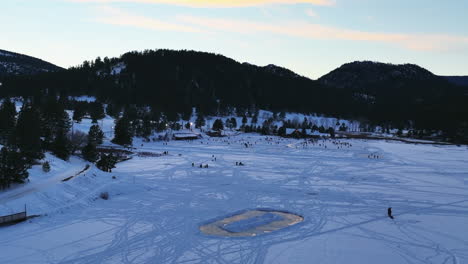 Evergreen-Lake-house-January-mid-winter-ice-skating,-pond-hockey-and-ice-fishing-under-lights-sunset-Colorado-cinematic-forward-motion