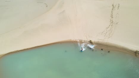 Sandboarding-from-sand-dune-to-small-lake-at-Te-Paki-Sand-Dunes,-New-Zealand-adventure,-drone-shot