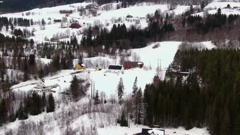 Rural-winter-area-with-houses-surrounded-by-snow,-hills-and-trees