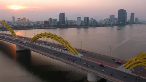 Amazing-colorful-wide-aerial-shot-of-iconic-Dragon-Bridge-Cau-Rong,-traffic-and-city-skyline-during-sunset-in-Danang,-Vietnam