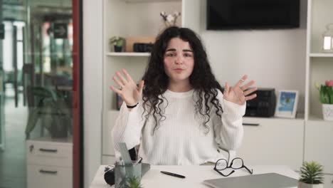 A-girl-is-sitting-at-a-table,-looking-directly-into-the-camera,-expressing-her-satisfaction,-emotively-gesturing-with-her-hands,-she-has-curly-black-hair,-dressed-in-casual-clothing