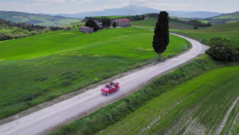 Aerial-of-red-car-driving-on-country-road-in-green-Tuscany-landscape