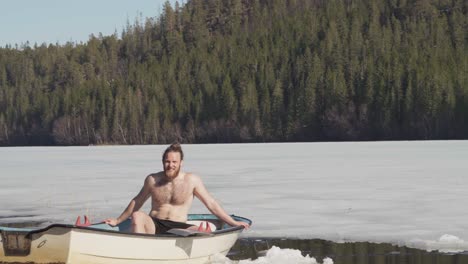 Shirtless-Man-Sitting-In-A-Boat-Afloat-On-Frozen-Lake-In-Winter