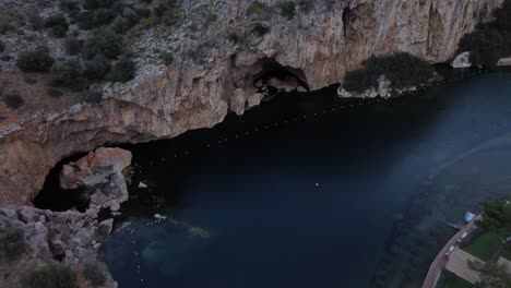 Aerial-view-of-the-submerged-lake-Vouliagmeni-in-Athens,-Greece-and-surrounding-cliffs-|-4K