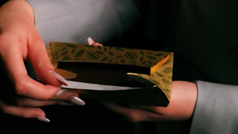 Top-view-of-a-woman's-hand-unwrapping-and-revealing-a-chocolate-bar-with-golden-packaging-on-black-background