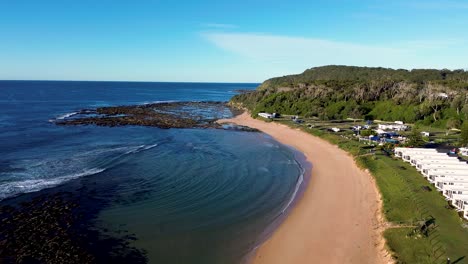 Drone-aerial-pan-shot-of-Bateau-Bay-Shelly-beach-huts-and-bushland-ocean-beach-travel-tourism-Central-Coast-NSW-Australia-4K