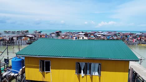 Close-up-drone-shot-of-a-unique-yellow-water-house-with-sea-skyline-and-houses-background,-at-Borneo---Pulau-Omadal,-Sabah,-Malaysia