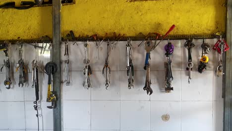 Selection-of-bike-tools-including-spanners,-wrench-and-screwdrivers-hanging-against-well-worn,-rustic-yellow-wall-in-bicycle-repair-shop
