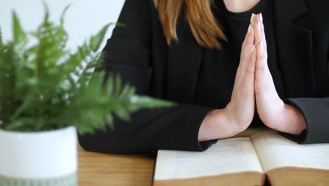 A-woman-praying-with-hands-held-flat-together-on-an-open-bible-book-on-a-table