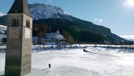 Aerial-View-Of-Submerged-Bell-Tower-At-Frozen-Lake-Reschen-With-High-Sun-Casting-Shadow