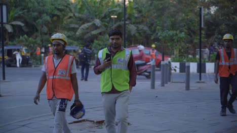 Two-Indian-male-construction-site-workers-in-safety-uniform-walking-through-the-road-after-work-shift-ends,-Bandra-Kurla-Complex,-Mumbai