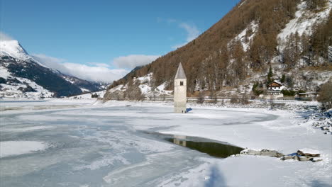 Aerial-View-Of-Submerged-Bell-Tower-At-Frozen-Lake-Reschen