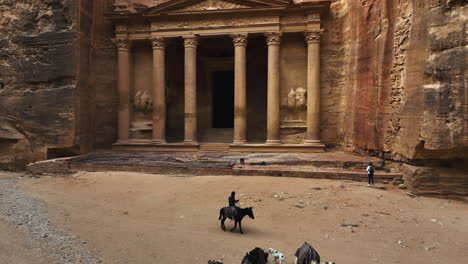 Camels-and-people-in-front-of-the-Treasury,-Al-Khazneh-mausoleum-in-Petra,-Jordan---aerial-view