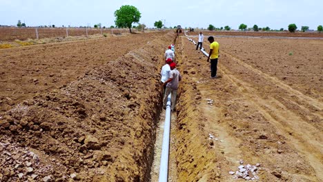 Indian-farmer-and-labor-working-on-the-water-pipeline-fittings-on-the-big-digging-land,-follow-shot-of-worker-working-in-the-farm